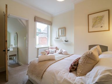 A bedroom with a bed a chair by the window and a dressing table in an adjacent area at Compass Cottage in Aldeburgh
