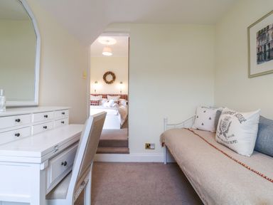 A small room with a white desk and chair on the left and a daybed with pillows on the right at Compass Cottage in Aldeburgh