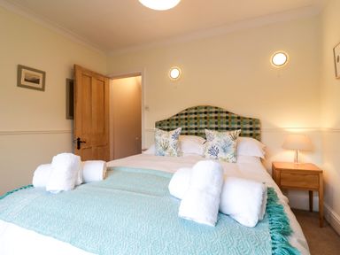 A bedroom with a bed with a checkered headboard white linens and rolled towels on a light blue throw at Compass Cottage in Aldeburgh