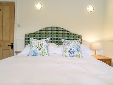 A bed with patterned pillows and a checkered headboard between two lamps at Compass Cottage in Aldeburgh
