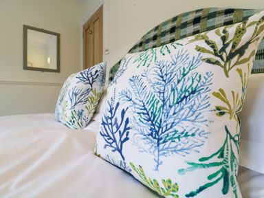 A close up of patterned pillows on a bed with a mirror and wooden door in the background at Compass Cottage in Aldeburgh