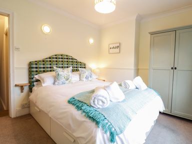 A bedroom with a double bed with patterned headboard and pillows and a wardrobe at Compass Cottage in Aldeburgh