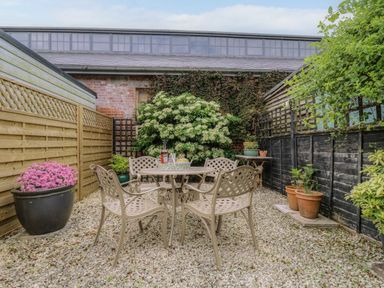 An outdoor patio with a round table and four chairs surrounded by plants and fences at Compass Cottage in Aldeburgh