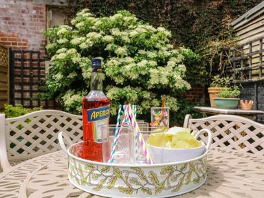 A garden table with a tray holding a bottle, glasses with straws, and a bowl of potato chips at Compass Cottage in Aldeburgh