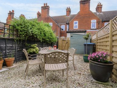 A small garden with a round table and four chairs on a gravel floor surrounded by fences and plants at Compass Cottage in Aldeburgh