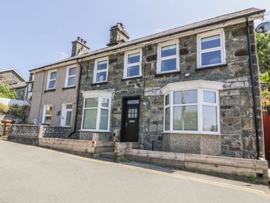 Two adjoining stone houses with bay windows and a black front door on a sloped street at Old Post Office in Blaenau Ffestiniog
