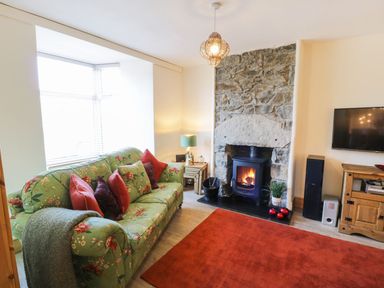 A living room with a floral sofa red pillows a stone fireplace with a stove and a red rug at Old Post Office in Blaenau Ffestiniog