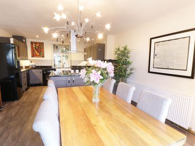 A dining area with a wooden table and gray chairs next to a kitchen with gray cabinets and a black refrigerator at Old Post Office in Blaenau Ffestiniog