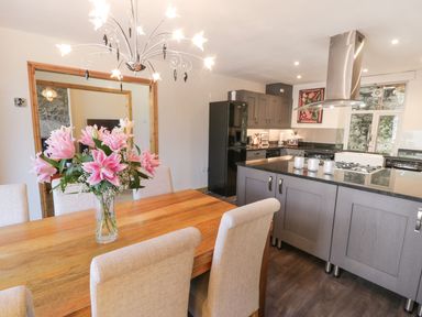 A kitchen with a wooden dining table with pink flowers and beige chairs at Old Post Office in Blaenau Ffestiniog