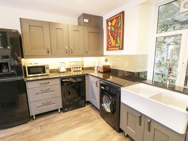 A kitchen with black appliances gray cabinets a large white sink and a window at Old Post Office in Blaenau Ffestiniog