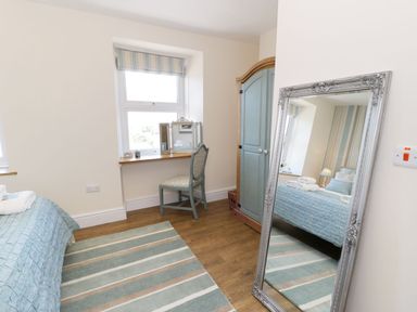 A bedroom with a bed a chair a vanity mirror a wardrobe a striped rug and a large standing mirror at Old Post Office in Blaenau Ffestiniog