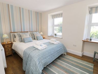 A bedroom with a double bed with blue and white bedding bedside tables with lamps two windows and striped wallpaper at Old Post Office in Blaenau Ffestiniog