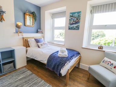 A bedroom with a single bed blue and white bedding two windows a chair and a wall-mounted lamp at Old Post Office in Blaenau Ffestiniog