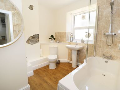 A bathroom with a bathtub shower combination toilet sink and round mirror at Old Post Office in Blaenau Ffestiniog