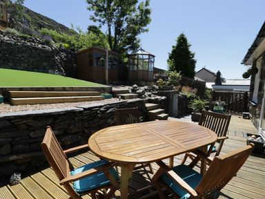 An outdoor wooden deck with a wooden table and four chairs with blue cushions at Old Post Office in Blaenau Ffestiniog
