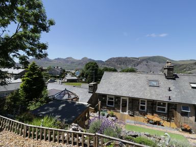 A backyard with a wooden deck table and chairs and plants around a stone house at Old Post Office in Blaenau Ffestiniog