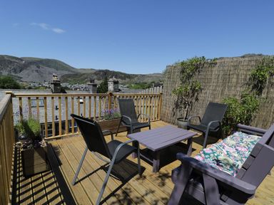 An outdoor wooden deck with chairs a small table and plants at Old Post Office in Blaenau Ffestiniog