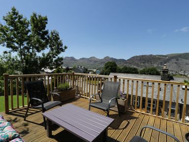 A wooden deck with black chairs and a table overlooking houses trees and mountains at Old Post Office in Blaenau Ffestiniog