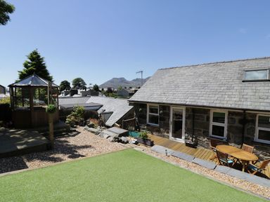 A garden with artificial grass gravel a wooden deck with a table and chairs a wooden gazebo and stone buildings with a mountain in the background at Old Post Office in Blaenau Ffestiniog