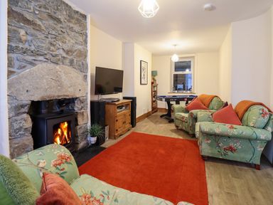 A living room with a stone fireplace wood stove television floral armchairs and a red rug at Old Post Office in Blaenau Ffestiniog