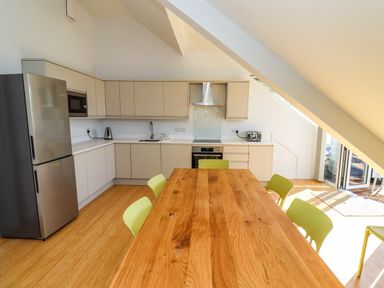 A kitchen with a wooden dining table and green chairs and white cabinets at Ocean View in Alnmouth