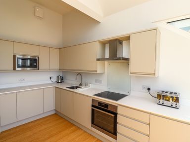 A kitchen with beige cabinets a microwave a kettle a sink a stove an oven a toaster and wooden floor at Ocean View in Alnmouth