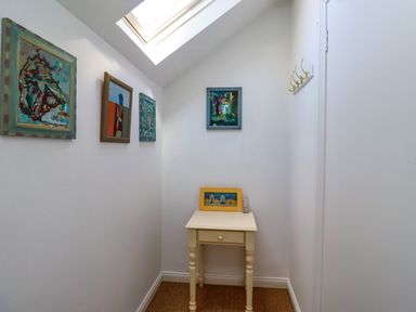 A small corner with a cream table under a skylight and four paintings on the walls at Ocean View in Alnmouth