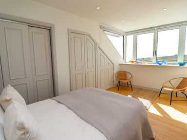 A bedroom with a bed gray blanket two woven chairs and windows with a view at Ocean View in Alnmouth
