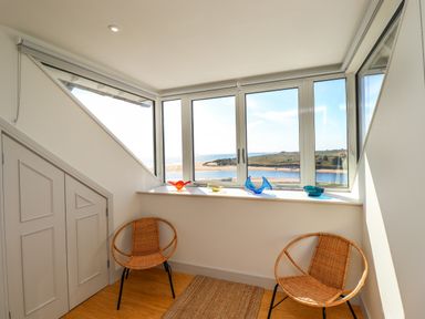A small seating area with two wicker chairs and decorative glass pieces on a window ledge overlooking a coastal landscape at Ocean View in Alnmouth
