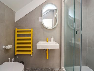 A bathroom with a yellow towel radiator a white sink and a glass shower enclosure at Ocean View in Alnmouth