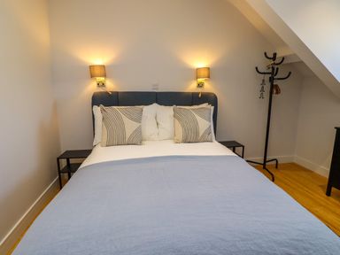 A bedroom with a double bed two bedside tables wall lamps and a coat rack at Ocean View in Alnmouth