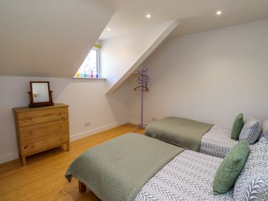 A bedroom with two single beds a wooden chest of drawers a mirror and a purple coat rack at Ocean View in Alnmouth