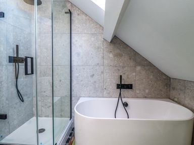 A bathroom with a walk in shower and a bathtub under a slanted ceiling at Ocean View in Alnmouth