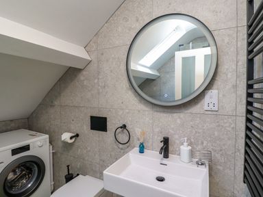 A bathroom with a washing machine sink and round mirror at Ocean View in Alnmouth