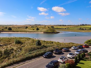 A coastal scene with parked cars on a road by a river and grassy fields at Ocean View in Alnmouth