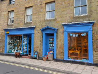 A stone building with blue window frames and two shop windows displaying various items at Ocean View in Alnmouth