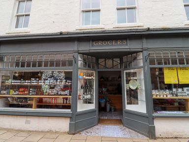 Exterior of a grocery store with open doors and display windows showing shelves of products at Ocean View in Alnmouth