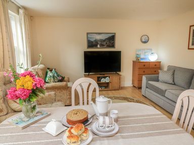 A living room with a dining table set with teapot and scones and a bouquet of flowers at Archie's in Minehead