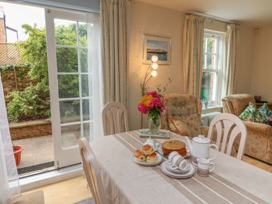 A dining table set with tea and cakes near a sliding glass door and armchairs at Archie's in Minehead