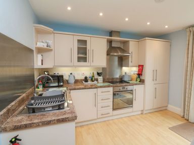 A kitchen with beige cabinets a stainless steel oven a stovetop a sink with a dish rack and various kitchen appliances at Archie's Minehead