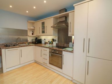 A kitchen with white cabinets a stove oven microwave kettle and a sink at Archie's Minehead