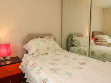 A bedroom with a bed with floral bedding a red bedside lamp and mirrored closet doors at Archie's in Minehead