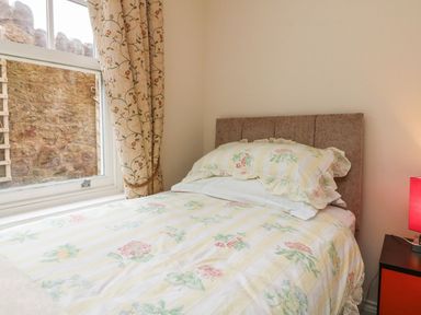 A bedroom with a bed covered in floral bedding next to a window with patterned curtains at Archie's in Minehead