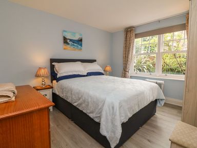 A bedroom with a double bed two bedside lamps a wooden dresser and a window showing plants outside at Archie's in Minehead