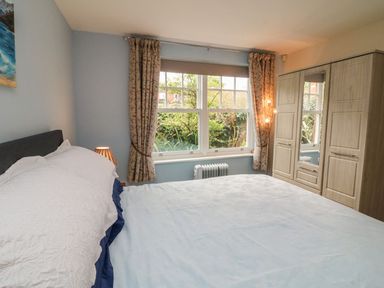 A bedroom with a bed near a window with floral curtains and a wooden wardrobe at Archie's in Minehead