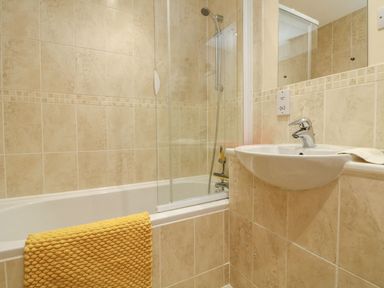 A bathroom with a bathtub a shower a sink and a yellow towel at Archie's in Minehead