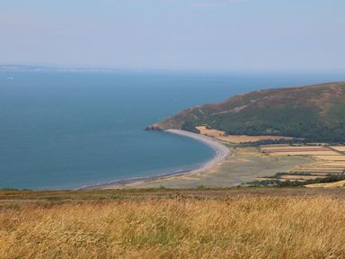 A coastal landscape with a curved beach hills and farmland at Archie's in Minehead
