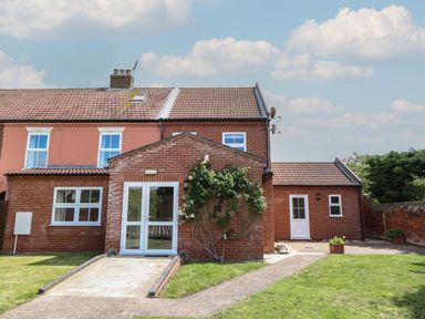 A brick house with multiple windows and doors a paved walkway and grass at Beach House in Winterton-On-Sea