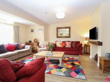 A living room with red and beige sofas a wooden coffee table and a colorful geometric rug at Beach House in Winterton-On-Sea