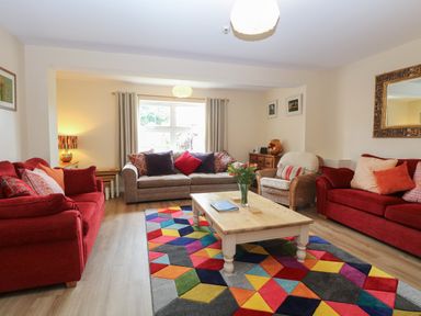 A living room with red sofas a wooden coffee table and a colorful geometric rug at Beach House in Winterton-On-Sea